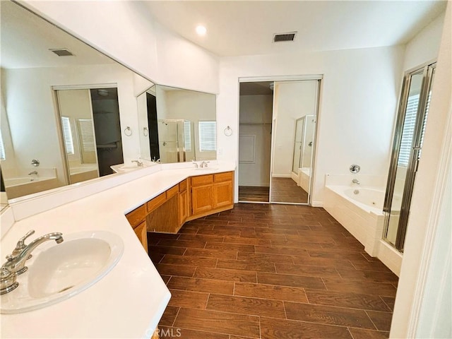 bathroom with double vanity, wood finish floors, a bath, and a sink