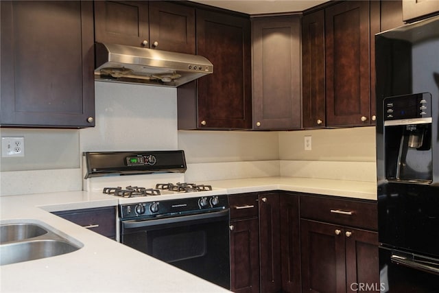 kitchen featuring under cabinet range hood, range with gas stovetop, and dark brown cabinetry