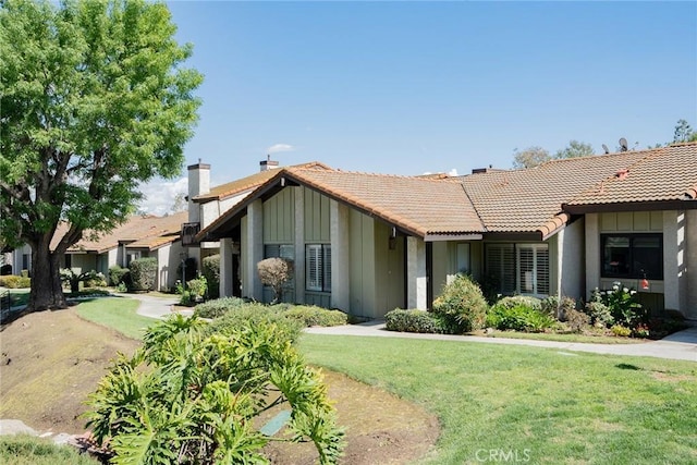 view of front of home featuring a tiled roof, a chimney, a front yard, and board and batten siding