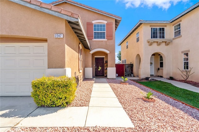 view of exterior entry featuring a tile roof, a gate, a garage, and stucco siding