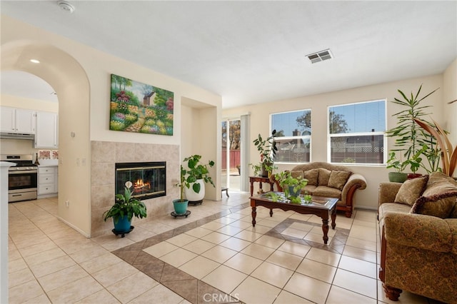 living room featuring light tile patterned floors, visible vents, a tile fireplace, and baseboards