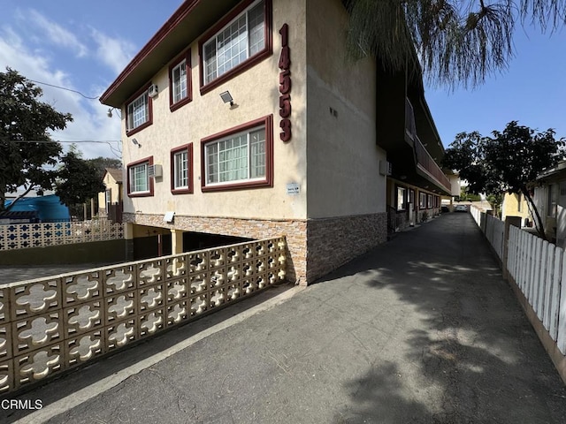 view of property exterior featuring fence, stone siding, and stucco siding