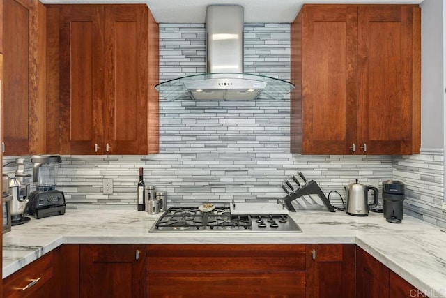 kitchen with wall chimney exhaust hood, light stone countertops, backsplash, and stainless steel gas cooktop