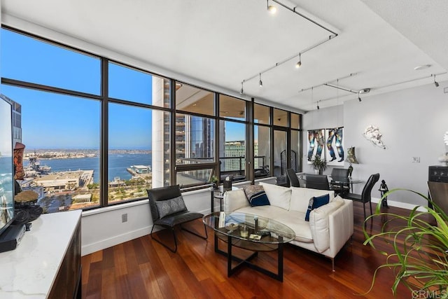 living area featuring track lighting, a water view, baseboards, and wood finished floors