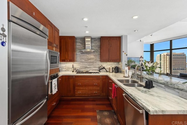 kitchen with a sink, backsplash, a peninsula, wall chimney range hood, and built in appliances