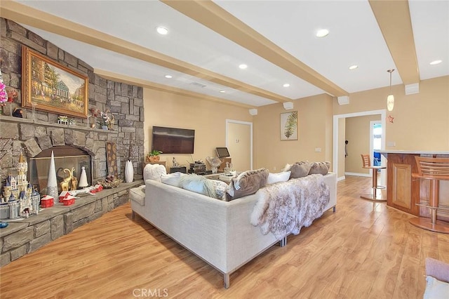 living area featuring wood finished floors, beam ceiling, recessed lighting, a stone fireplace, and a bar