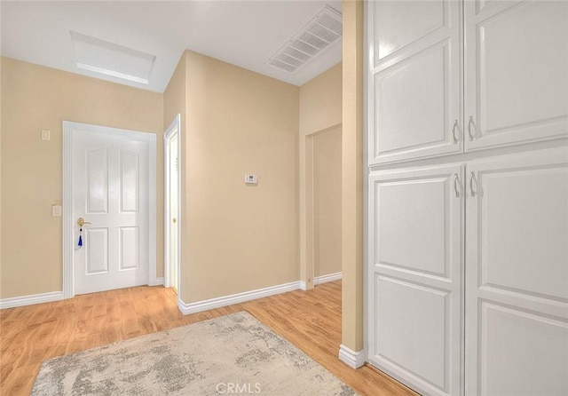 hall featuring visible vents, baseboards, light wood-style floors, and attic access