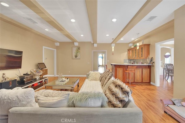 living room featuring beam ceiling, visible vents, light wood-type flooring, and a wealth of natural light