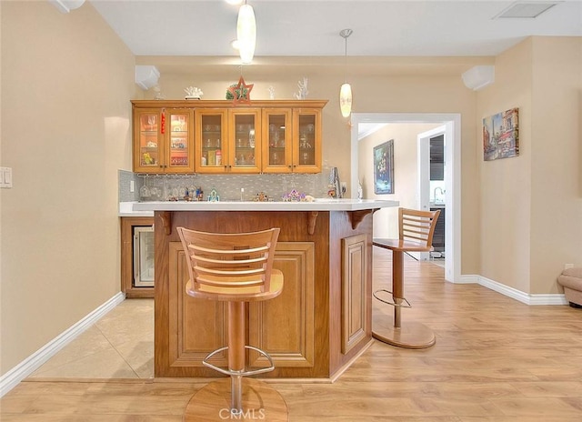 bar featuring light wood-style flooring, tasteful backsplash, indoor wet bar, baseboards, and hanging light fixtures