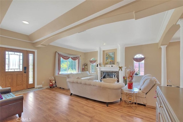 living area featuring baseboards, decorative columns, ornamental molding, light wood-style floors, and a glass covered fireplace