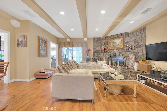 living area with visible vents, beam ceiling, a stone fireplace, light wood finished floors, and baseboards