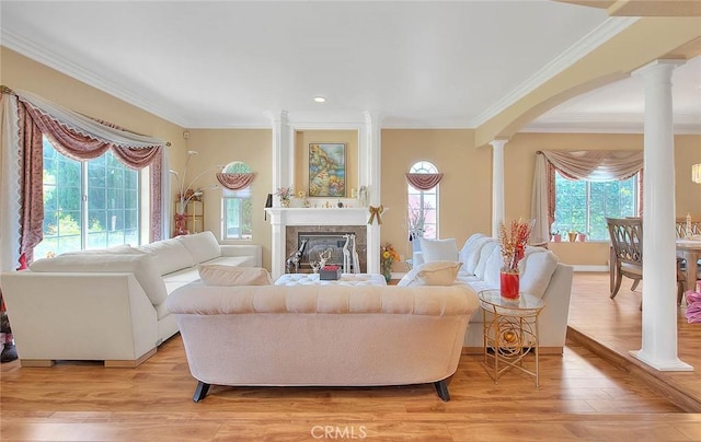 living room with ornate columns, arched walkways, a glass covered fireplace, crown molding, and light wood-type flooring