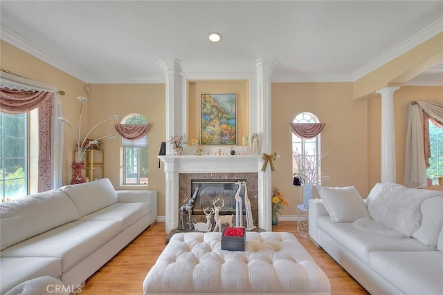 living room featuring a high end fireplace, crown molding, light wood-style floors, and decorative columns