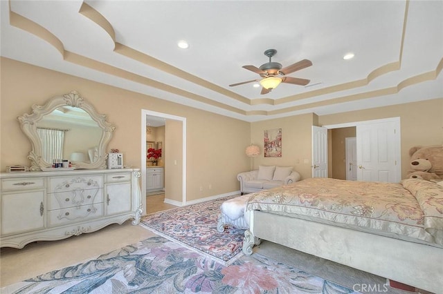 bedroom with baseboards, a tray ceiling, light carpet, recessed lighting, and ensuite bath