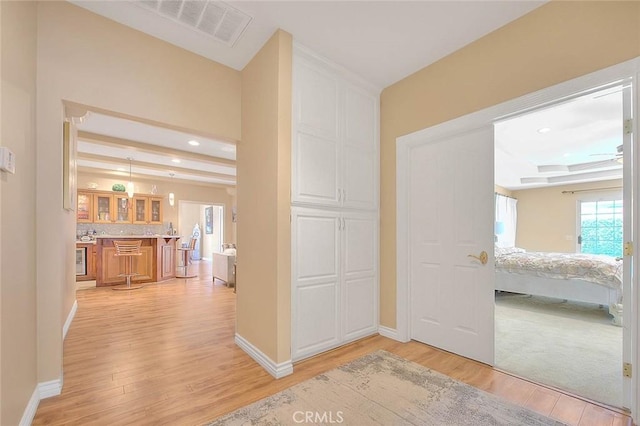 hall with visible vents, baseboards, and light wood-style flooring