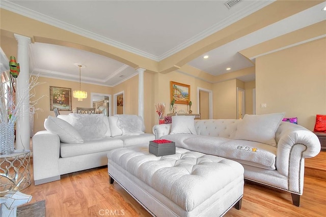 living area featuring visible vents, ornamental molding, light wood-style flooring, arched walkways, and ornate columns