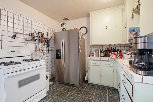 kitchen with tile counters, stainless steel fridge, backsplash, and white gas range