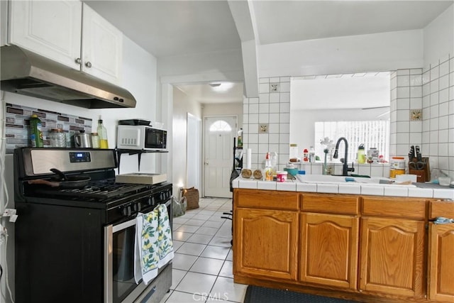 kitchen featuring stainless steel gas range oven, under cabinet range hood, tile countertops, light tile patterned floors, and a sink