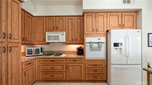 kitchen with visible vents, brown cabinets, white appliances, a toaster, and light stone countertops
