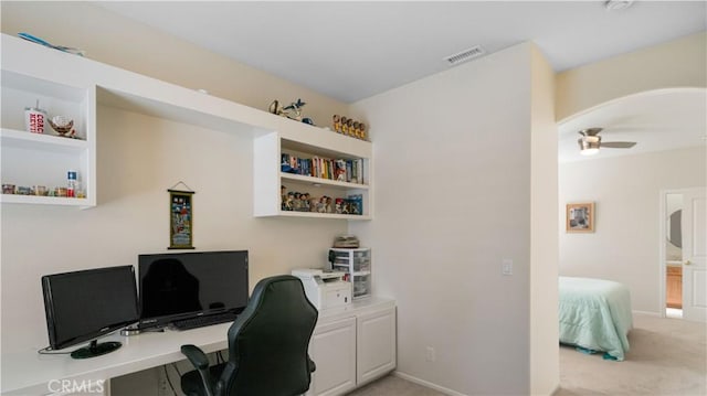 office space with light carpet, visible vents, arched walkways, and a ceiling fan