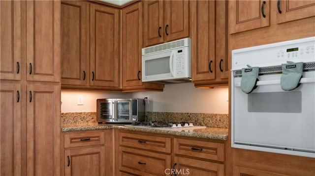 kitchen featuring white appliances, brown cabinets, a toaster, and light stone countertops