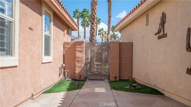 exterior space with stucco siding, a patio, a tile roof, and a gate
