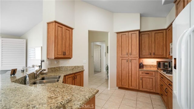 kitchen with white appliances, light stone counters, brown cabinetry, and a sink