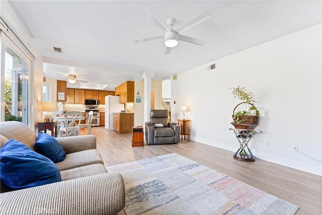 living room featuring visible vents, light wood-style floors, ceiling fan, and decorative columns