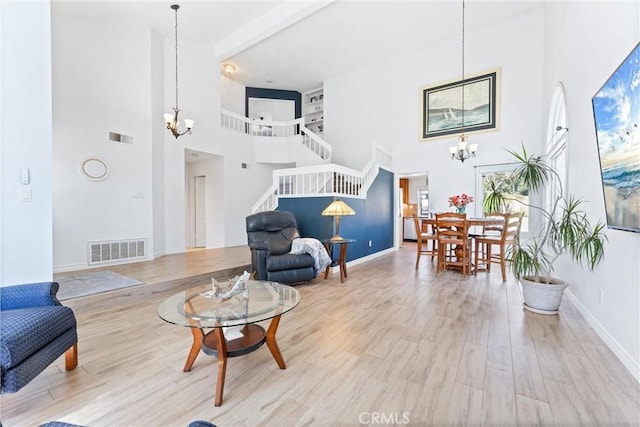 living area with visible vents, a notable chandelier, wood finished floors, and stairway