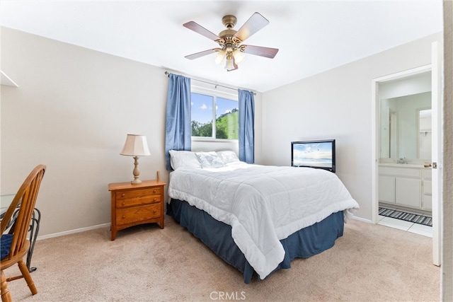 bedroom featuring baseboards, ceiling fan, light colored carpet, ensuite bath, and a sink