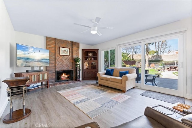 living area with a brick fireplace, ceiling fan, and wood finished floors