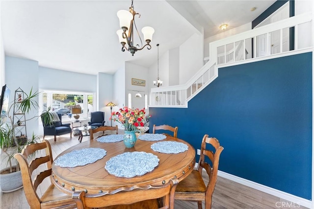 dining area featuring high vaulted ceiling, wood finished floors, baseboards, a chandelier, and stairs