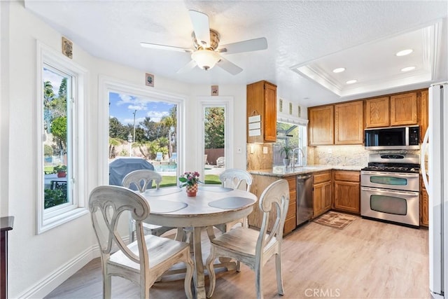 kitchen with brown cabinetry, backsplash, stainless steel appliances, and light wood-type flooring