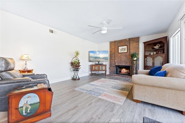 living area featuring wood finished floors, baseboards, visible vents, a ceiling fan, and a fireplace