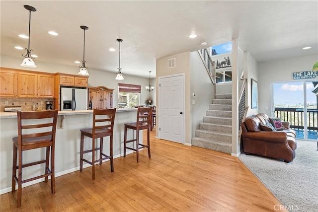 kitchen with light wood-type flooring, visible vents, a breakfast bar, backsplash, and stainless steel fridge with ice dispenser