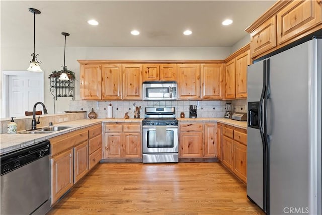 kitchen featuring light wood-style flooring, a sink, tasteful backsplash, stainless steel appliances, and hanging light fixtures