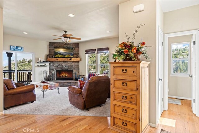 living room featuring recessed lighting, a stone fireplace, light wood finished floors, baseboards, and ceiling fan