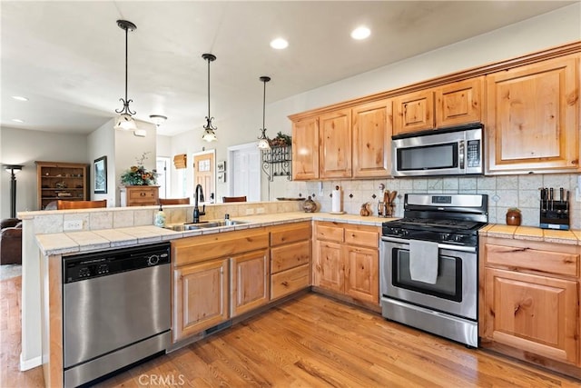 kitchen with light wood finished floors, a peninsula, a sink, appliances with stainless steel finishes, and backsplash