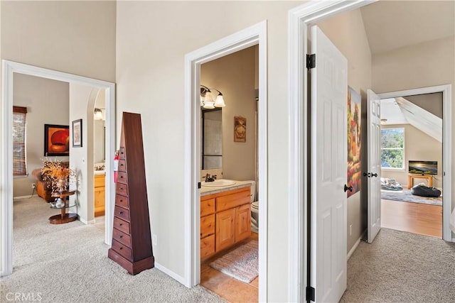 corridor with light carpet, arched walkways, baseboards, and a sink