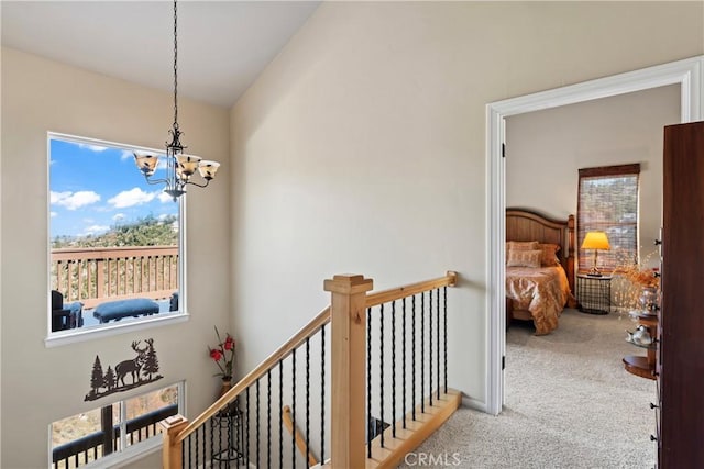 hallway with a notable chandelier, an upstairs landing, carpet, and lofted ceiling