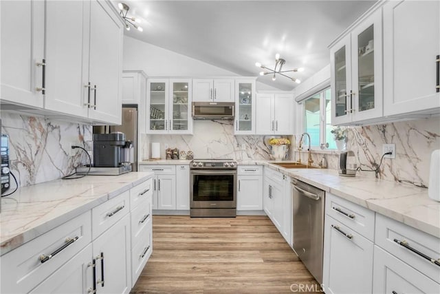 kitchen featuring vaulted ceiling, stainless steel appliances, light wood-style floors, white cabinetry, and a sink