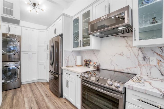 kitchen featuring stainless steel appliances, stacked washer and dryer, visible vents, and white cabinetry