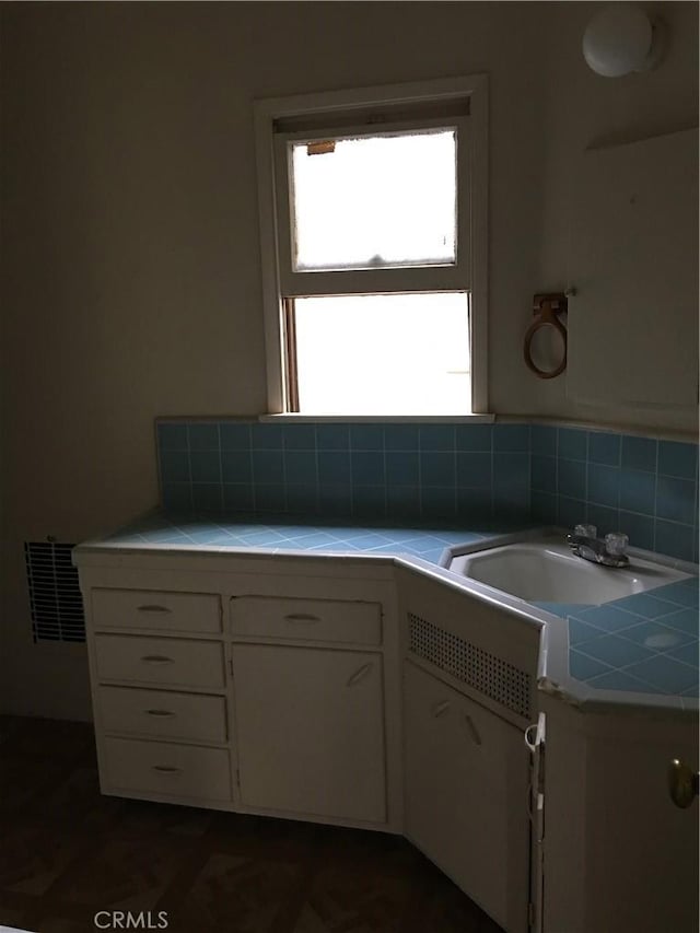 kitchen featuring a sink, visible vents, tile counters, and white cabinets