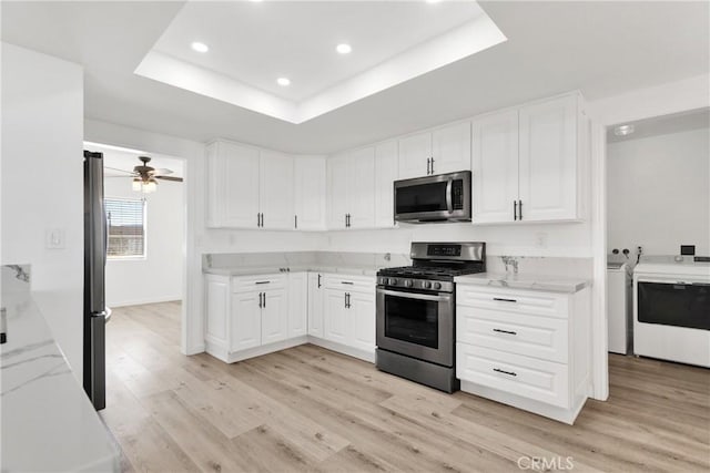 kitchen featuring light stone counters, stainless steel appliances, a raised ceiling, washing machine and dryer, and light wood-type flooring