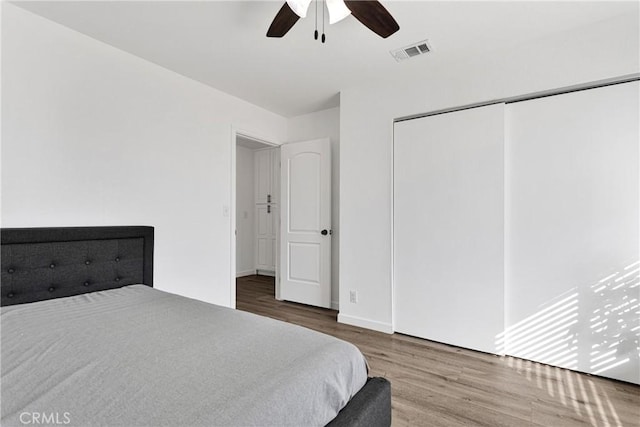 bedroom with visible vents, baseboards, ceiling fan, wood finished floors, and a closet