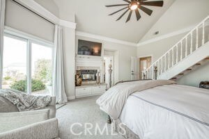 carpeted bedroom featuring ceiling fan, high vaulted ceiling, and a fireplace with raised hearth