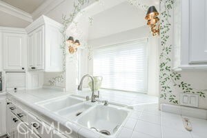 kitchen with a sink, white cabinets, tile patterned flooring, and ornamental molding