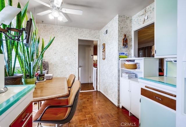 kitchen with visible vents, white cabinets, wallpapered walls, tile counters, and ceiling fan