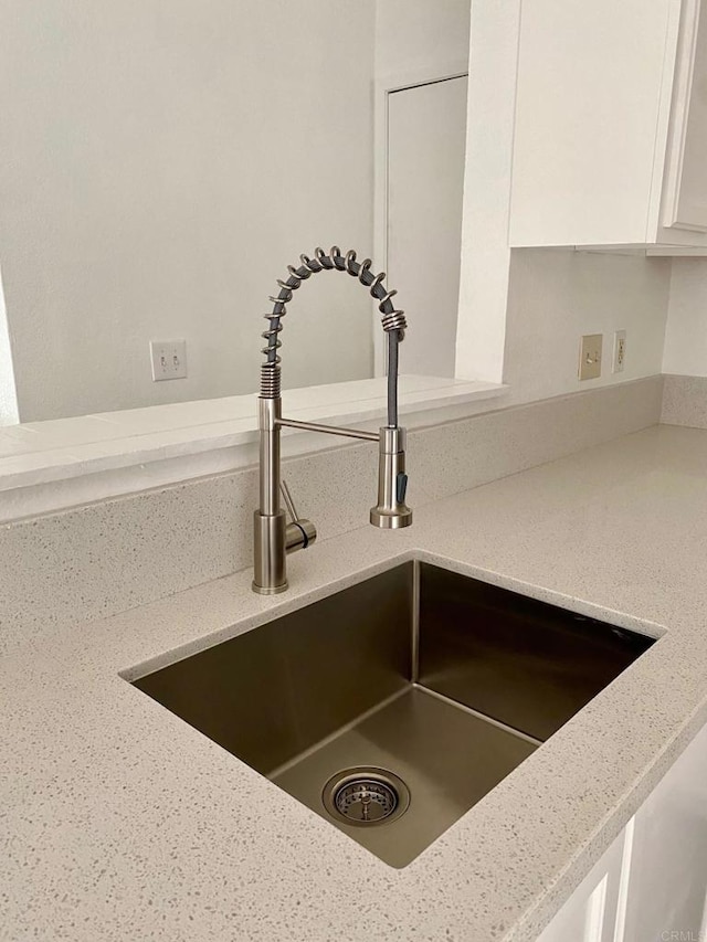 interior details featuring light stone counters, white cabinets, and a sink