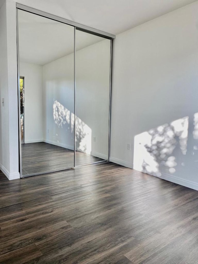 unfurnished bedroom featuring dark wood finished floors, baseboards, and a closet